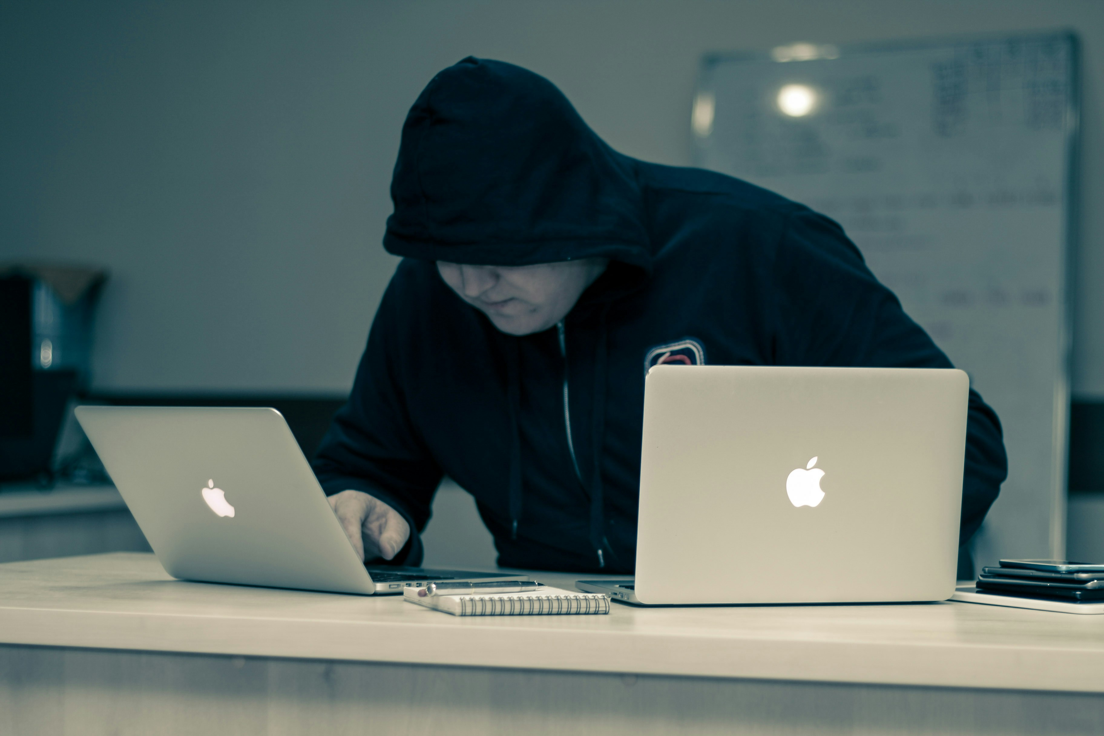 A cybecrimminal in front of two MacBooks.